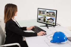 Young Female Architect Looking At Designs Of House On Computer In Office